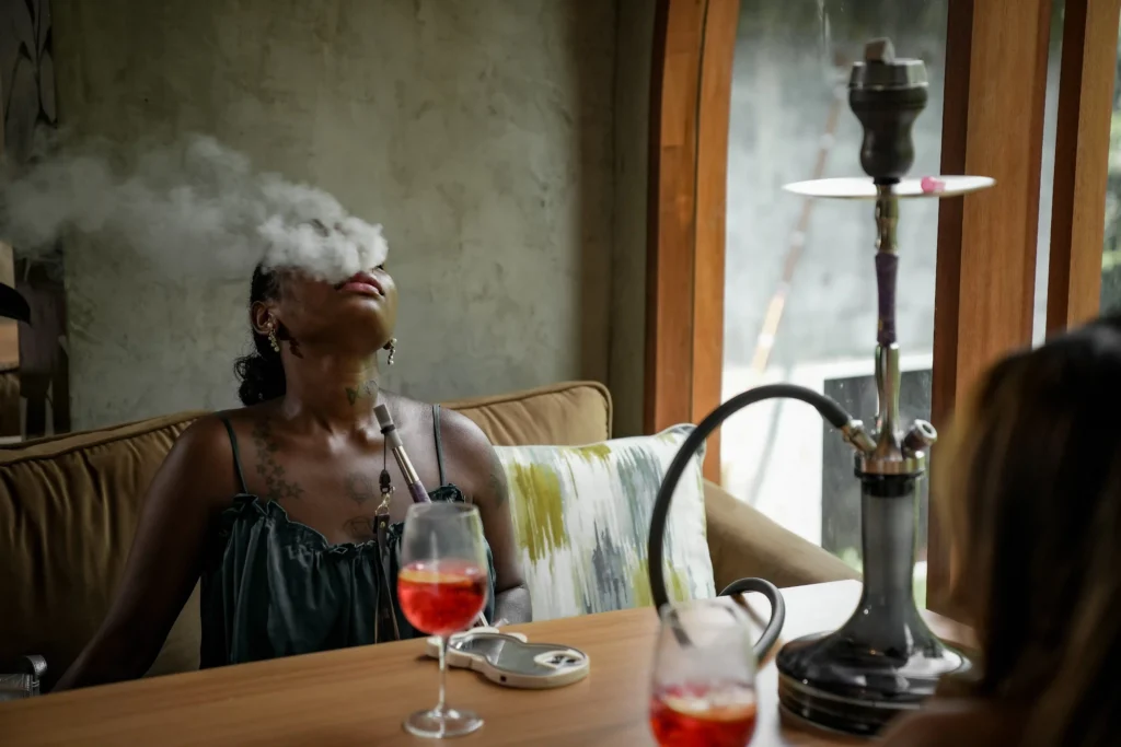 A relaxed guest exhaling a thick cloud of shisha smoke next to a refreshing drink. Experience premium hookah sessions when exploring where to smoke & buy Tangiers in Bali.