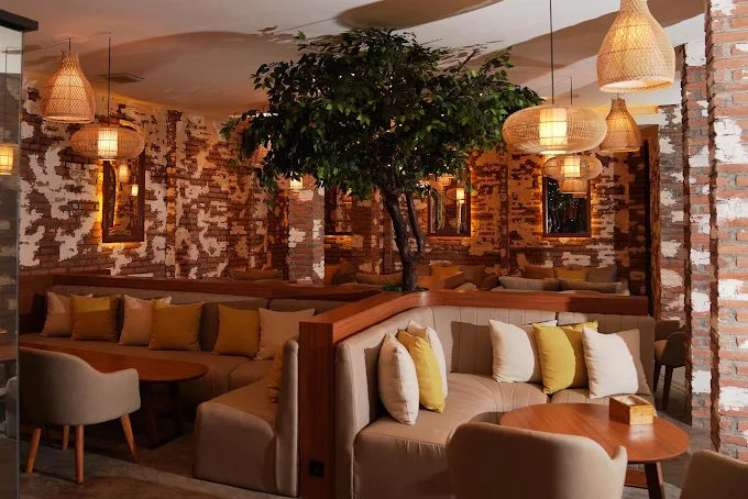 A cozy, modern-boho lounge featuring exposed brick walls, plush booth seating, and a decorative indoor tree at Eden Seminyak. A premium destination when searching for where to smoke & buy Tangiers in Bali.