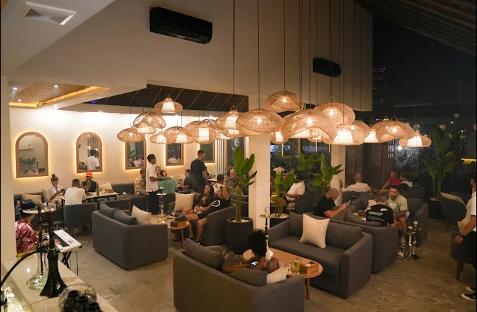 A lively crowd relaxing on comfortable sofas under beautiful woven lamps at Eden Canggu. If you want a social atmosphere while discovering where to smoke & buy Tangiers in Bali, this energetic lounge hits the mark.