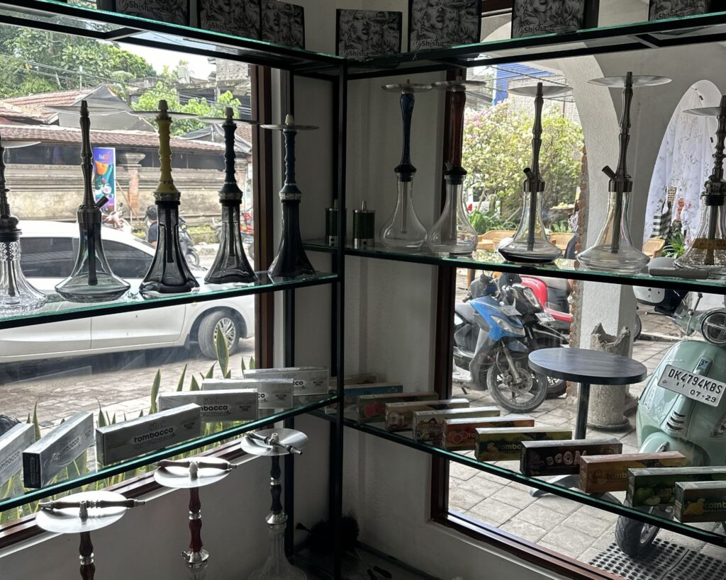 Glass shelves displaying premium hookah pipes and tobacco boxes by the window at MyShisha Ubud. This official store is your go-to answer for where to smoke & buy Tangiers in Bali.