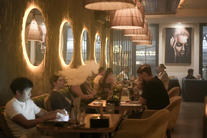 Guests working and enjoying a hookah session in a stylish, dimly lit lounge with glowing wall mirrors. A top choice when looking for where to smoke & buy Tangiers in Bali.